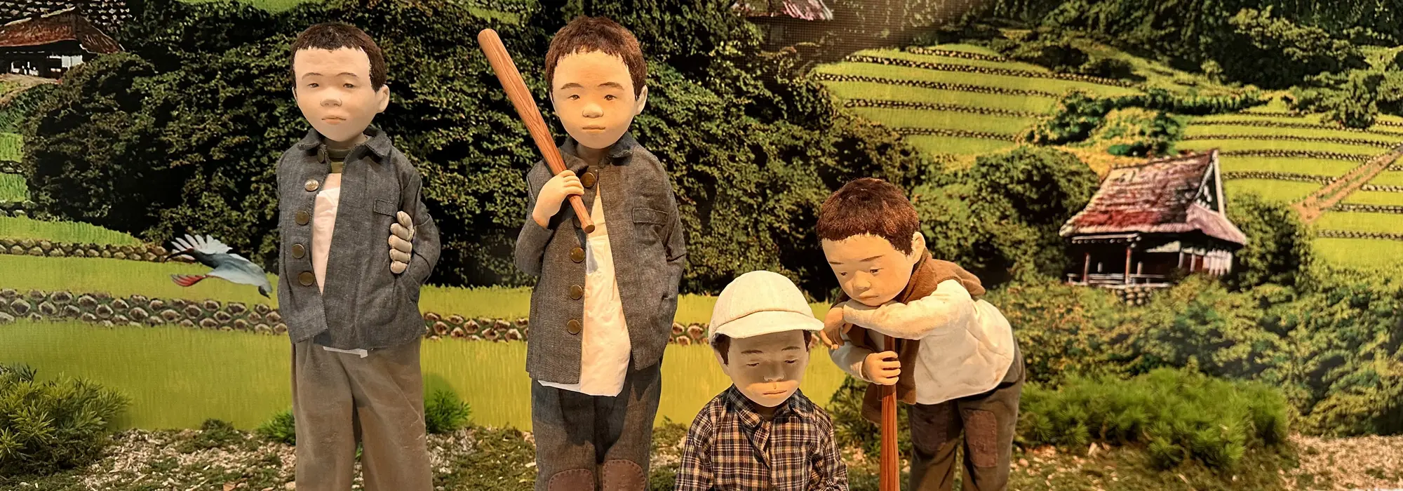 棚田と茅葺きの家を背に集まる、男の子たちの人形