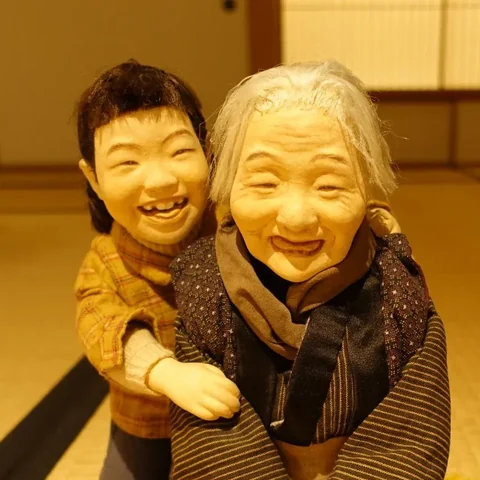 作品「仏笑」の、笑うおばあちゃんと、背中から抱きつく孫の人形