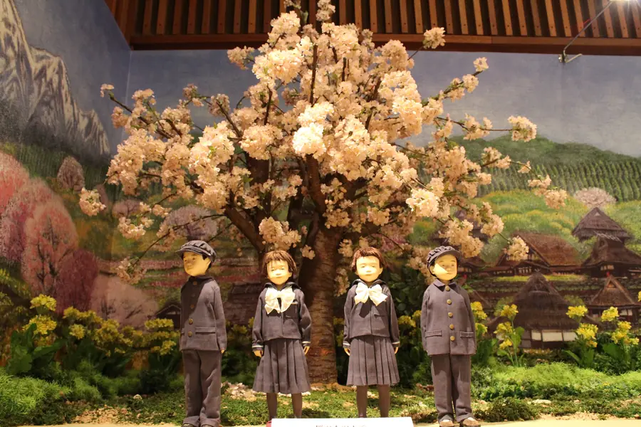満開の桜の前に並ぶ、制服姿のこどもたちの人形