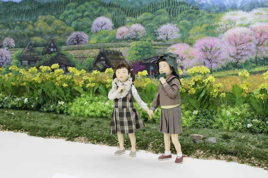 菜の花畑の前で手をつなぐ、ふたりの女の子の人形
